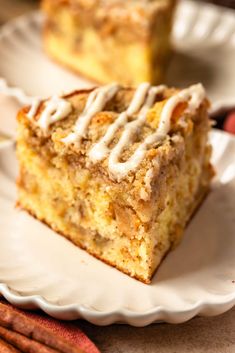 two slices of cinnamon coffee cake on white plates with cinnamon sticks next to it and an orange napkin in the background