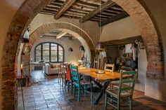 an arched doorway leads to a dining room with brick walls and flooring, along with a wooden table surrounded by colorful chairs