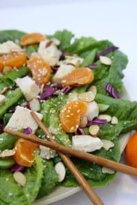 salad with oranges, almonds and dressing on a white plate next to chopsticks