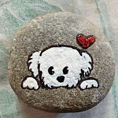 a white dog with a red heart on it's face painted on a rock