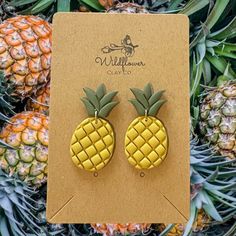 a pair of pineapple earrings sitting on top of a pile of pineapples