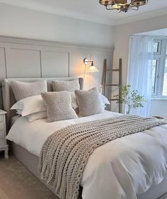 a bed with white linens and pillows in a bedroom next to a large window