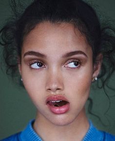 a young woman with her mouth open wearing a blue shirt and pearl earrings is looking at the camera