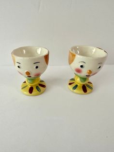 two cups with faces painted on them sitting next to each other in front of a white background