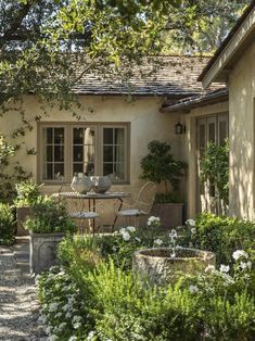 a patio with chairs and tables in front of a house surrounded by greenery, shrubs and trees