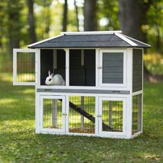 a rabbit in a small white and black house on the grass with trees in the background