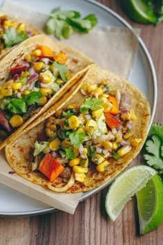 two tacos on a plate with limes and cilantro