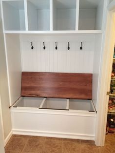 a white bench with wooden seat and hooks on it's back wall in a kitchen