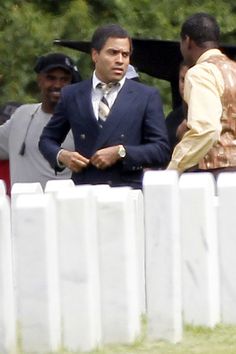 a man in a suit and tie standing next to a white fence with other men behind him