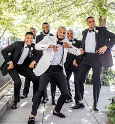 a group of men in tuxedos posing for a photo on the sidewalk with their arms around each other