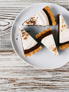 four pieces of pie on a plate with white and brown icing, sitting on a wooden table