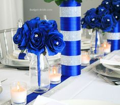 blue roses are in vases and candles on a table set for a formal dinner