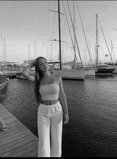 black and white photo of woman in cropped top standing on dock next to sailboats