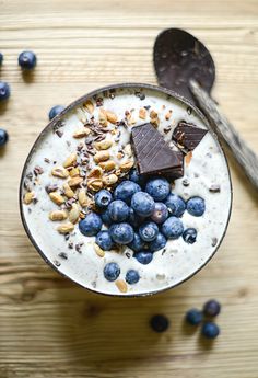 a bowl filled with cereal and blueberries on top of a wooden table next to spoons