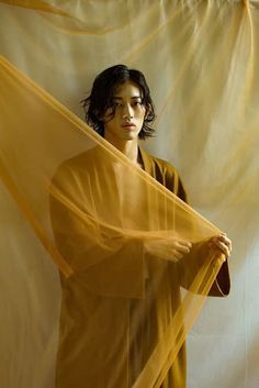 a young man is standing in front of a white backdrop holding a yellow cloth over his head