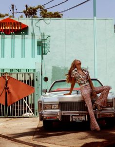 a woman leaning on the hood of a car in front of a building with a neon sign