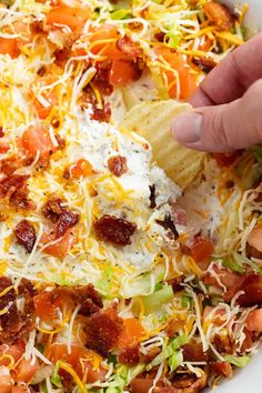 someone is dipping some tortilla chips into a bowl full of shredded cheese and vegetables