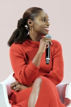 a woman sitting in a white chair holding a microphone and talking to someone on the other side