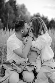 a man and woman kissing while sitting on the ground in front of some tall grass