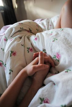 a person laying in bed with white sheets and pink flowers on the comforter, holding their hands together