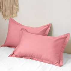 two pink pillows sitting on top of a bed next to a wall hanging with tassels