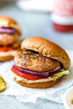 two hamburgers with lettuce, tomato and pickles on the table next to some ketchup