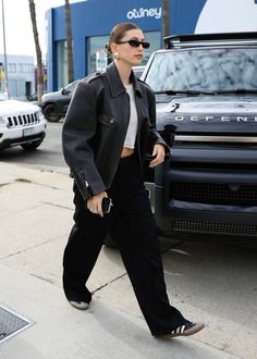 a woman walking down the street in front of a black truck with sunglasses on her head