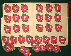 an open book with red apples on it and letters cut out to spell the alphabet