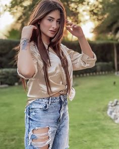 a woman with long hair wearing ripped jeans and a tan shirt is posing for the camera