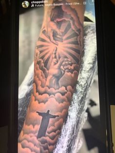 a person with a tattoo on their arm and the image of jesus in the clouds