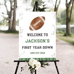 a welcome sign for a football themed baby's first year down ceremony with flowers and greenery