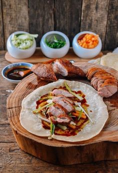 a tortilla with meat, vegetables and sauces on a wooden board next to other foods