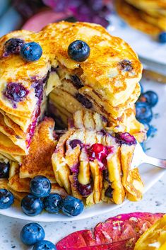 a stack of pancakes with blueberries and orange slices on a white plate next to some fruit