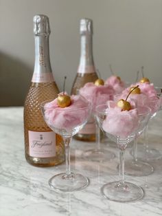 three wine glasses filled with ice cream and topped with cherries next to a bottle of champagne