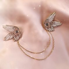 two gold angel brooches with chains attached to them on a pink satin background