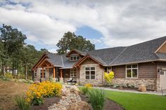 a large house with stone and wood accents in the front yard, surrounded by flowers