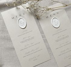 two wedding menus are sitting on a table with flowers in the middle and one is white