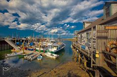 several boats are docked in the water near a dock with a cloudy sky above them