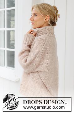 a woman standing in front of a window wearing a sweater