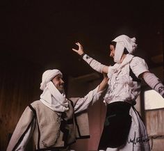 two people dressed in costume standing next to each other with their hands out and one holding his head