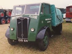 an old green truck parked on top of a grass covered field next to other trucks