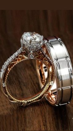 two wedding rings with diamond accents on top of each other, sitting on a wooden surface