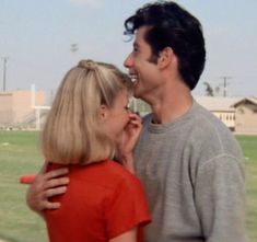 a man and woman standing next to each other in front of a field with grass