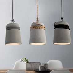 three pendant lights hanging over a wooden table with white chairs and a vase on it