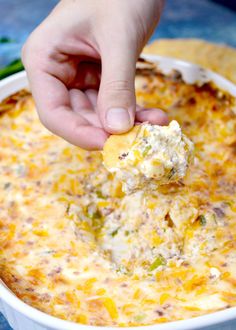 a hand dipping a cracker into a casserole dish