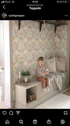 a little boy sitting on top of a bed next to a wallpapered room