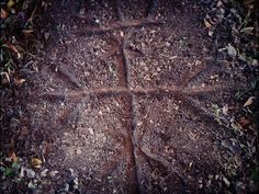 a cross made out of dirt on the ground with leaves and grass around it, as seen from above