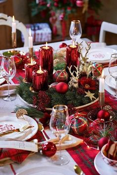 the table is set for christmas dinner with red and gold decorations, candles and plates