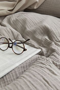 a pair of glasses sitting on top of a bed next to an open book and blanket