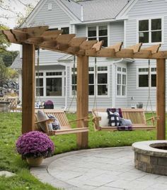 a wooden porch swing sitting next to a fire pit in front of a gray house